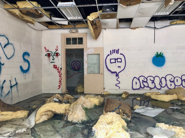 Ein Raum mit Graffiti an den Wänden, eine Tür im Hintergrund, Deckenleuchten und verstreute Gegenstände auf dem Boden, die tragische Ereignisse im Detroit-Bereich symbolisieren.