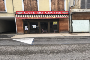 Außenansicht eines Gebäudes mit einer 'Cafe du Centre'-Tafel, Fenstern, einer Tür und einer Straße davor mit einer Texttafel.