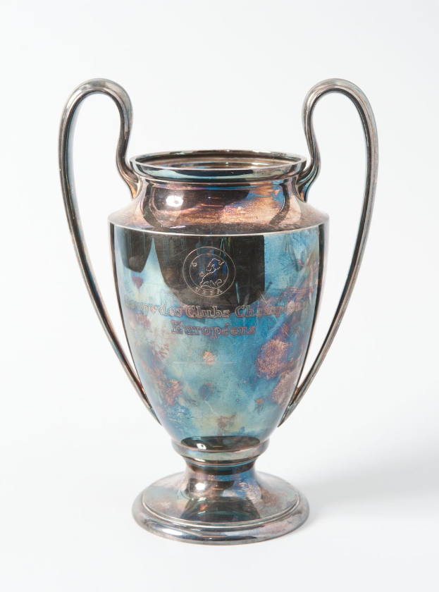 Der UEFA Champions League Pokal, ein silberner und blauer Stahlbecher mit zwei Händeln, der mit «UEFA Champions League» beschriftet ist, vor einem weißen Hintergrund.