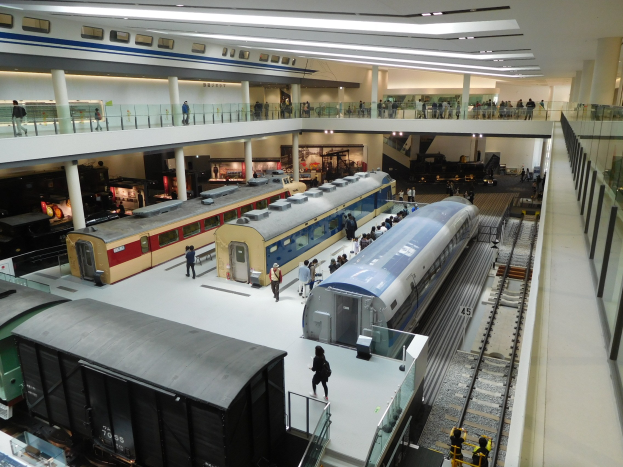 Ein großer Museumsraum mit verschiedenen Bahnen in unterschiedlichen Größen und Farben, mit Menschen, die sie vom Boden, Geländern und Säulen unter Deckenlampen beobachten.