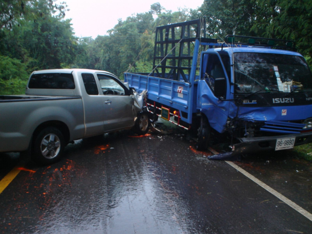 Ein geschädigter LKW mit eingedrückter Front und verbeulter Karosserie am Straßenrand, umgeben von Bäumen unter einem klaren blauen Himmel.