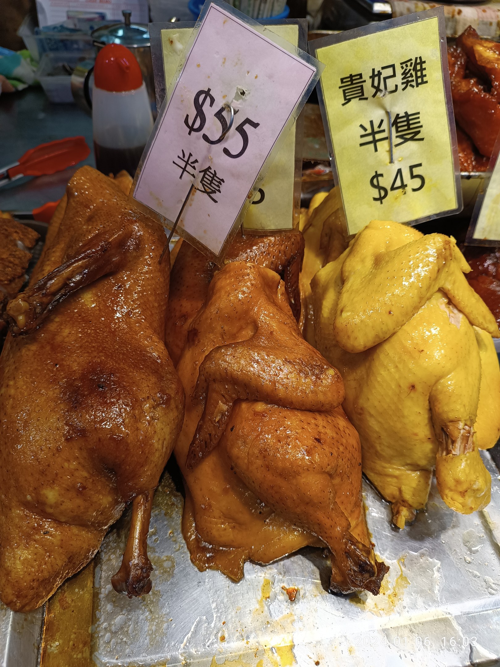 Hühner auf einem Metalltablett mit Preisschildern in einem belebten Markt.