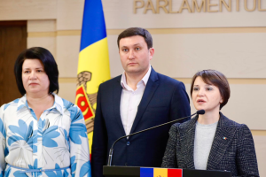 Zwei Frauen und ein Mann stehen an einem Podium vor einer ukrainischen Flagge, wobei der Mann ein schwarzes Sakko, ein weißes Hemd und schwarze Hosen trägt und die Frau rechts ein aschfarbenes Kleid trägt und über die Ukraine-Krise diskutieren.